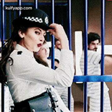 A Woman In A Police Uniform Is Standing In Front Of A Jail Cell . GIF