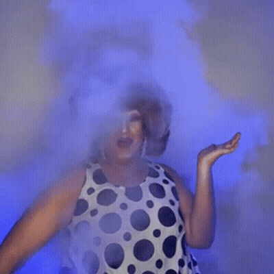 A Woman In A Polka Dot Dress Is Dancing In A Room With Smoke Coming Out Of Her Face . GIF