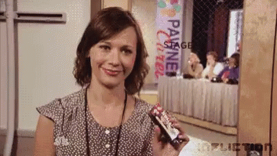 A Woman In A Polka Dot Shirt Is Smiling While Holding A Snickers Bar . GIF