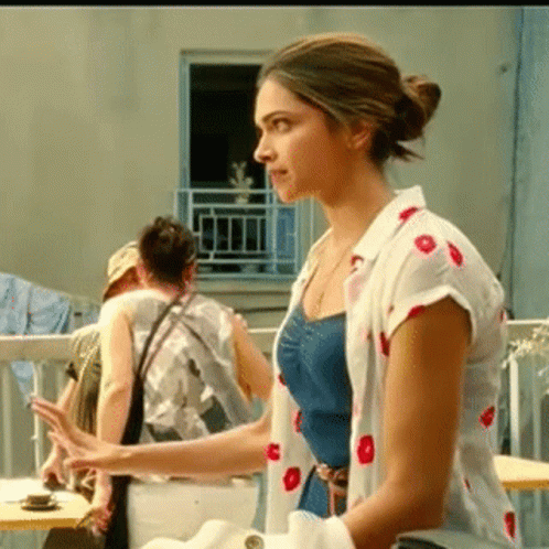 A Woman In A Polka Dot Shirt Is Standing On A Balcony . GIF