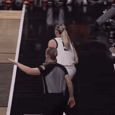 A Woman In A Ponytail Stands Next To A Referee GIF