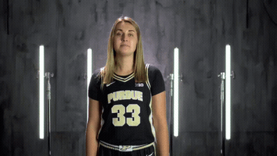 A Woman In A Purdue Jersey Stands In Front Of A Row Of Lights GIF