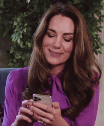 A Woman In A Purple Blouse Is Smiling While Looking At Her Phone GIF