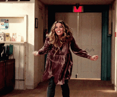 A Woman In A Purple Dress Is Dancing In A Hallway With A Red Exit Sign Above Her GIF