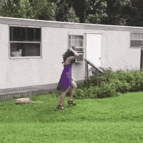 A Woman In A Purple Dress Is Dancing In Front Of A White Trailer . GIF