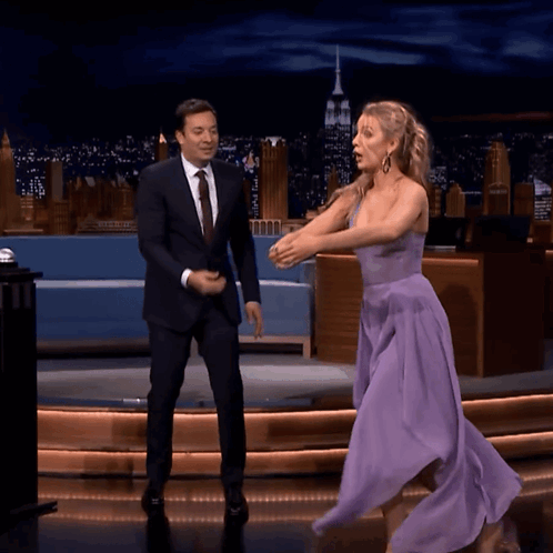 A Woman In A Purple Dress Is Dancing On A Stage With A Man In A Suit GIF