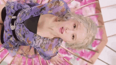 A Woman In A Purple Dress Is Laying On Her Stomach On A Pink Surface . GIF