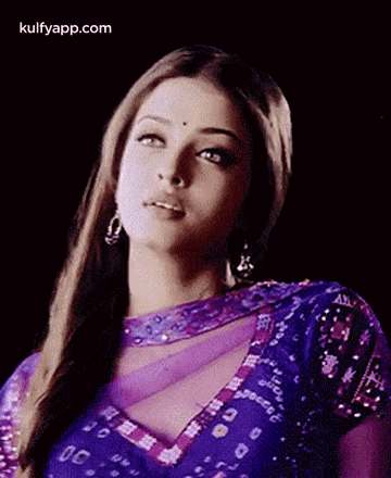 A Woman In A Purple Dress Is Looking At The Camera . GIF