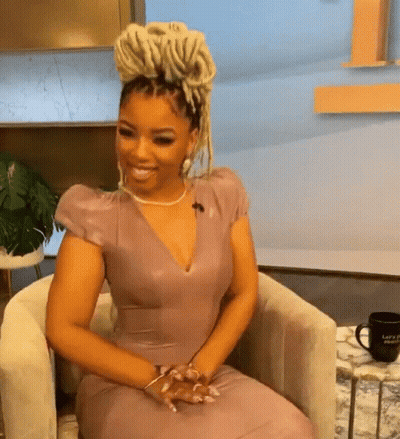 A Woman In A Purple Dress Is Sitting In A Chair And Smiling GIF