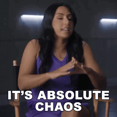 A Woman In A Purple Dress Is Sitting In A Director 'S Chair And Saying It 'S Absolute Chaos GIF