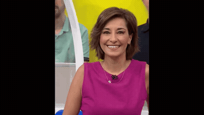 A Woman In A Purple Dress Is Smiling In Front Of A Yellow Wall . GIF