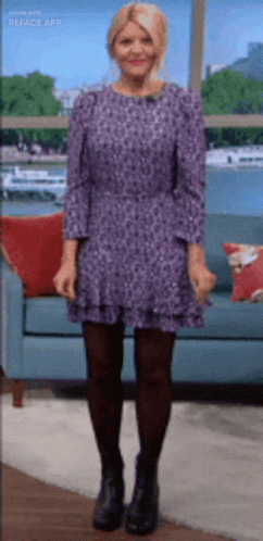 A Woman In A Purple Dress Is Standing In Front Of A Blue Couch . GIF