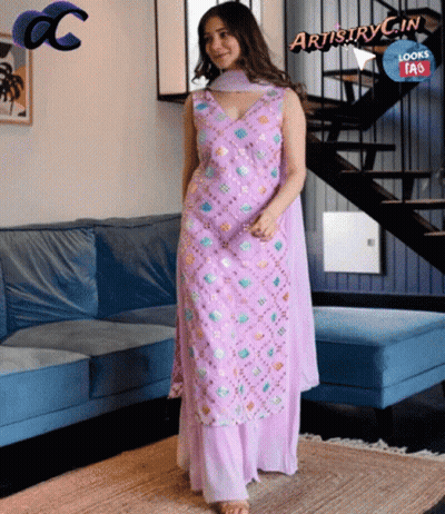 A Woman In A Purple Dress Is Standing In Front Of A Blue Couch GIF