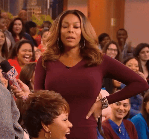 A Woman In A Purple Dress Is Standing In Front Of A Crowd Holding A Microphone GIF