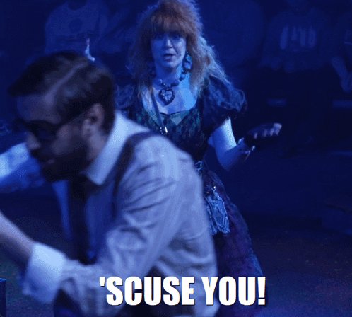 A Woman In A Purple Dress Is Standing In Front Of A Man With The Words Scuse You Written On The Bottom GIF