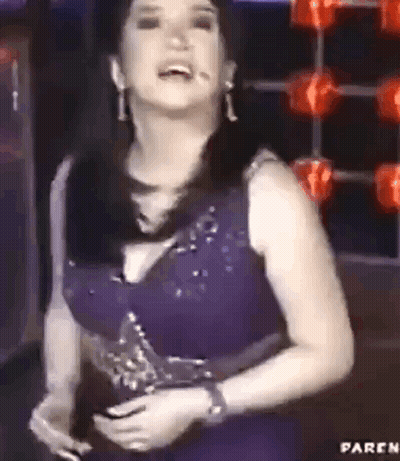 A Woman In A Purple Dress Is Standing In Front Of A Microphone And Holding A Trophy . GIF