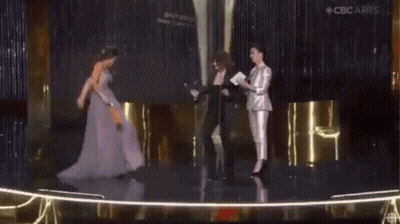 A Woman In A Purple Dress Is Standing On A Stage Holding A Trophy . GIF