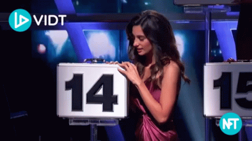 A Woman In A Purple Dress Is Touching A Sign That Says 14 GIF