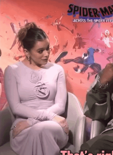 A Woman In A Purple Dress Sits In Front Of A Spider-Man Poster GIF