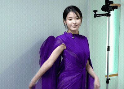 A Woman In A Purple Dress Stands Next To A Camera GIF