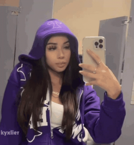 A Woman In A Purple Hoodie Is Taking A Selfie In A Mirror . GIF