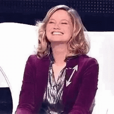 A Woman In A Purple Jacket Is Smiling And Sitting On A White Chair . GIF