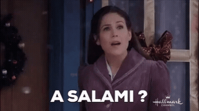 A Woman In A Purple Jacket Is Standing In Front Of A Door And Smiling . GIF