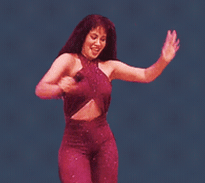 A Woman In A Purple Jumpsuit Is Holding A Microphone And Dancing GIF