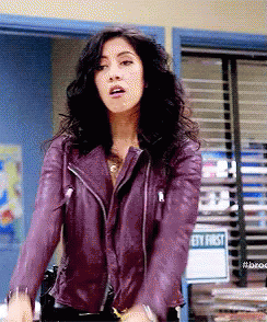 A Woman In A Purple Leather Jacket Is Standing In Front Of A Window . GIF