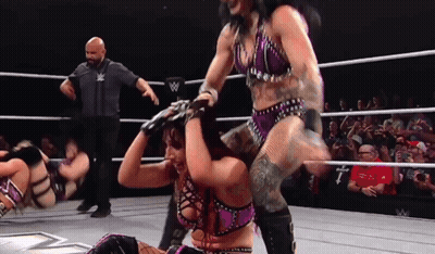 A Woman In A Purple Outfit Is Being Lifted By A Man In A Wrestling Ring GIF