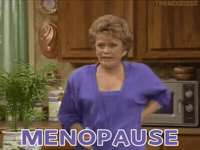 A Woman In A Purple Robe Is Standing In A Kitchen And Says " Menopause " GIF