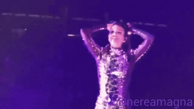 A Woman In A Purple Sequined Dress Is Standing On A Stage In Front Of A Microphone .. GIF