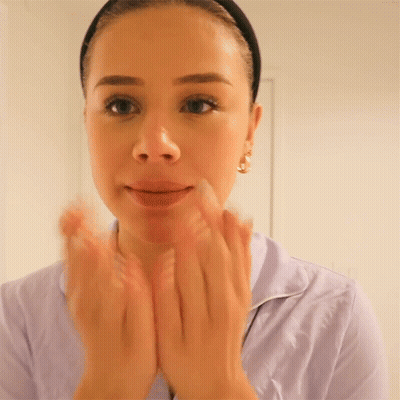 A Woman In A Purple Shirt Is Clapping Her Hands In Front Of Her Face GIF