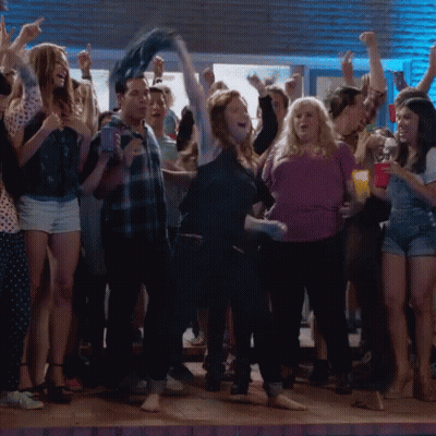 A Woman In A Purple Shirt Is Dancing In A Crowd Of People GIF