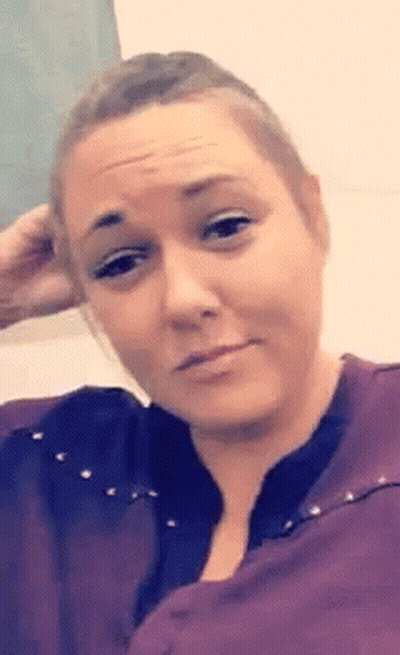 A Woman In A Purple Shirt Is Making A Funny Face And Holding Her Hand To Her Head . GIF