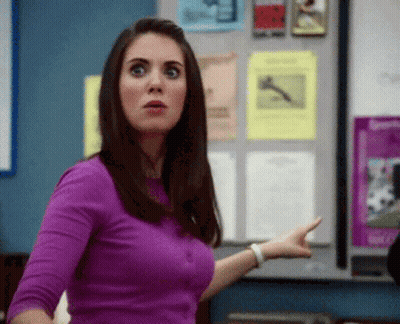 A Woman In A Purple Shirt Is Pointing At Something In Front Of A Bulletin Board GIF