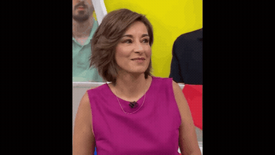 A Woman In A Purple Shirt Is Sitting In Front Of A Yellow Wall . GIF