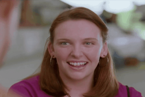 A Woman In A Purple Shirt Is Smiling With Her Teeth Showing GIF