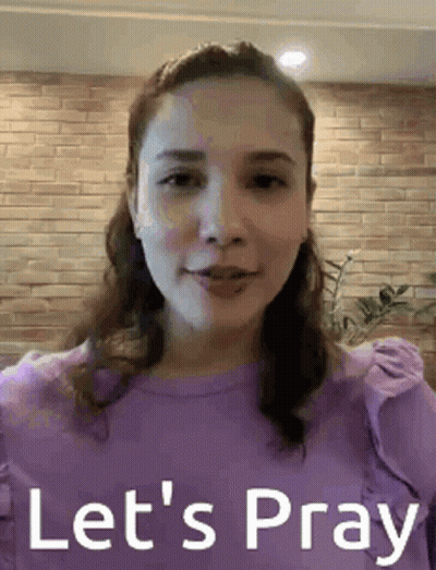 A Woman In A Purple Shirt Is Standing In Front Of A Brick Wall . GIF