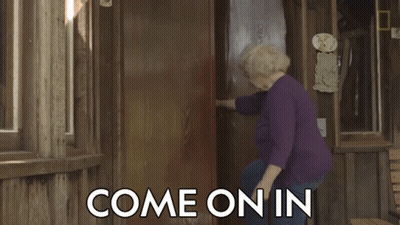 A Woman In A Purple Shirt Is Standing In Front Of A Door That Says Come On In On It GIF