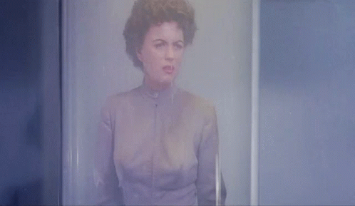 A Woman In A Purple Shirt Is Standing In Front Of A Glass Door GIF