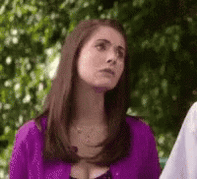 A Woman In A Purple Shirt Is Standing In Front Of A Tree And Looking Up . GIF