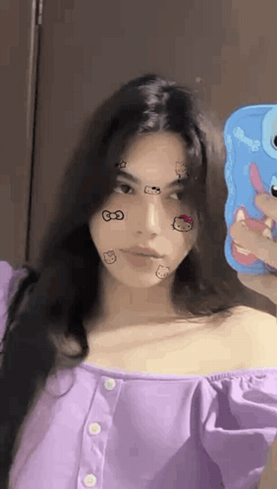 A Woman In A Purple Shirt Is Taking A Selfie With Her Phone . GIF