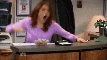 A Woman In A Purple Shirt Is Yawning At A Desk . GIF