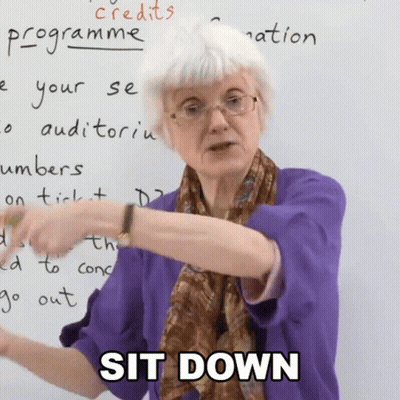 A Woman In A Purple Shirt Says Sit Down In Front Of A Whiteboard GIF