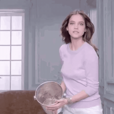 A Woman In A Purple Sweater Is Holding A Bucket Of Water In Her Hands . GIF