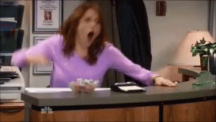A Woman In A Purple Sweater Is Yawning While Sitting At A Desk . GIF