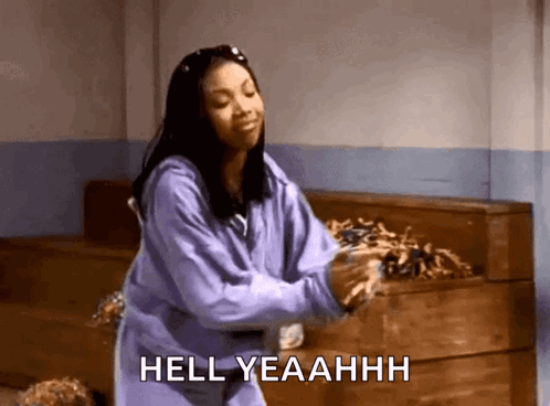 A Woman In A Purple Sweatshirt Is Dancing In A Room With The Words Hell Yeahhh Written Below Her . GIF