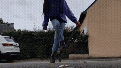 A Woman In A Purple Sweatshirt Is Riding A Skateboard On The Street GIF