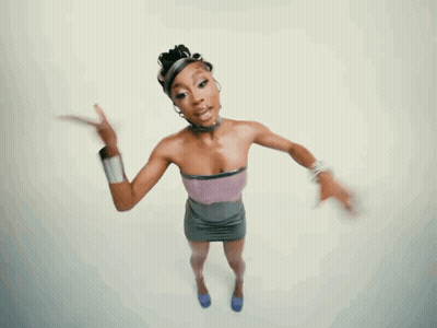 A Woman In A Purple Top And Gray Skirt Is Pointing GIF